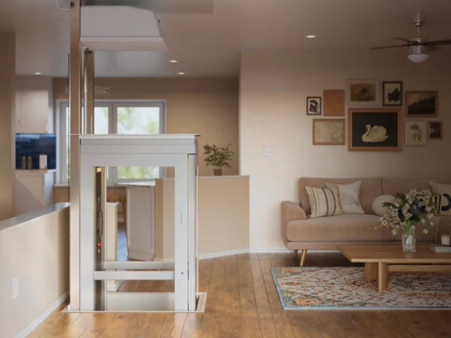 Modern pitless residential elevator installed in an open-concept living room, featuring a compact self-supporting white cabin with glass panels, integrated into hardwood flooring for seamless multi-level home accessibility.