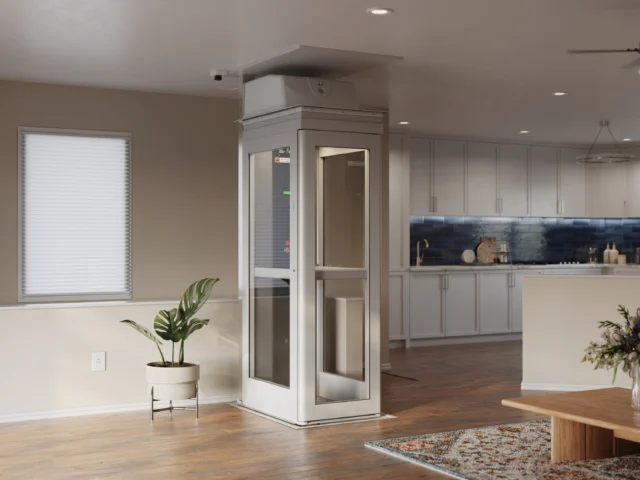 A white, compact residential elevato sits at the lower level of a bright home, beside a clean kitchen.