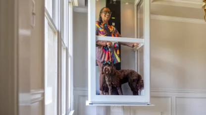 Homeowner riding a compact glass residential elevator with her dog inside a bright home interior, illustrating accessible aging-in-place mobility.