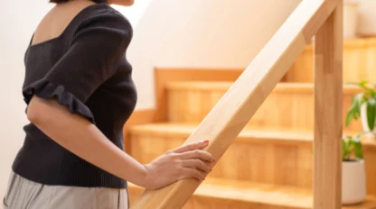 A woman in a black shirt faces away from the camera as she starts climbing the steps, her hand on the rail.