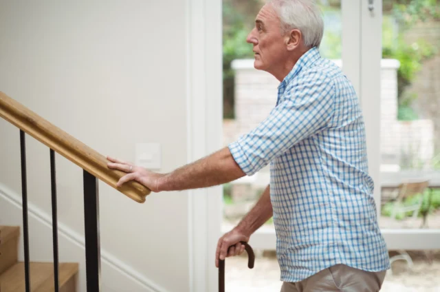 Older man holding the hook of his cane while looking up the stairs nervously.