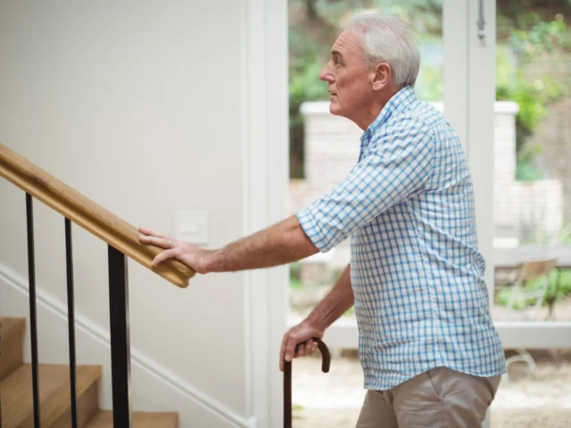 Older man holding the hook of his cane while looking up the stairs nervously.