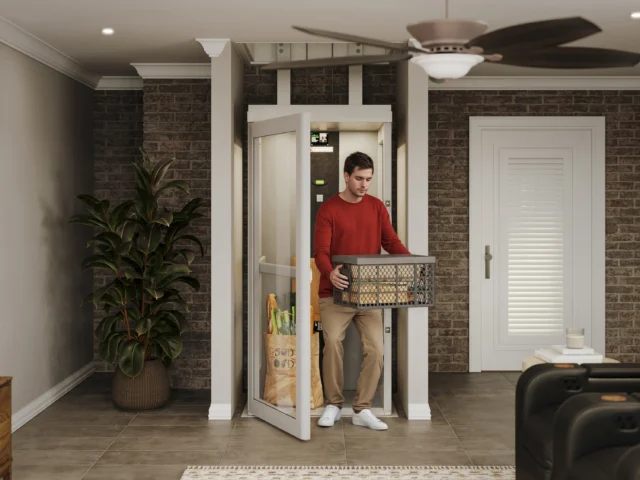 Young man in a red shirt exits a tan home elevator, carrying a full laundry basket.