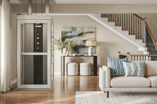 A white home elevator parked in a bright, decorated living room with stairs leading to the second floor in the background.